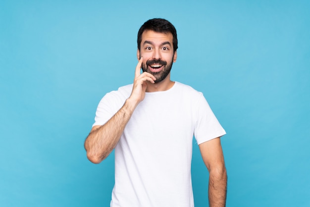 Young man with beard  over isolated blue with surprise and shocked facial expression