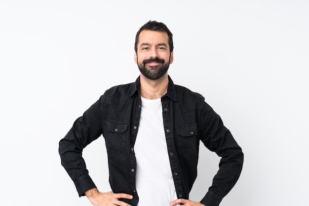 Young man with beard over isolated white  posing with arms at hip and smiling