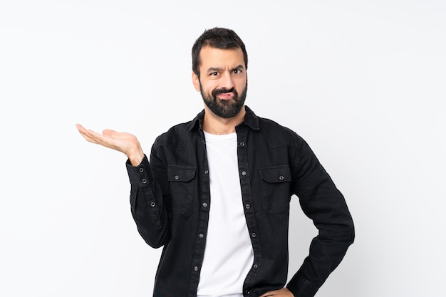 Young man with beard over isolated white  unhappy for not understand something