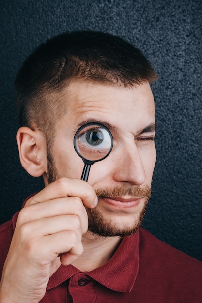 A young man with a beard looks through a magnifying glass. 