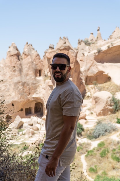 Young man with beard and sunglasses in the foreground with the typical houses built in the rock of the Cappadocia area in the background