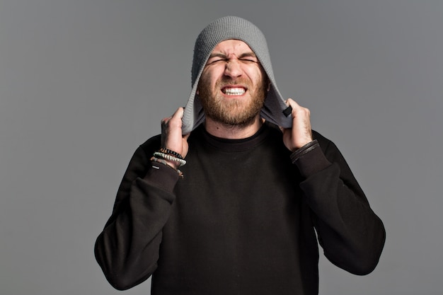 A young man with a beard wearing a hat on a gray