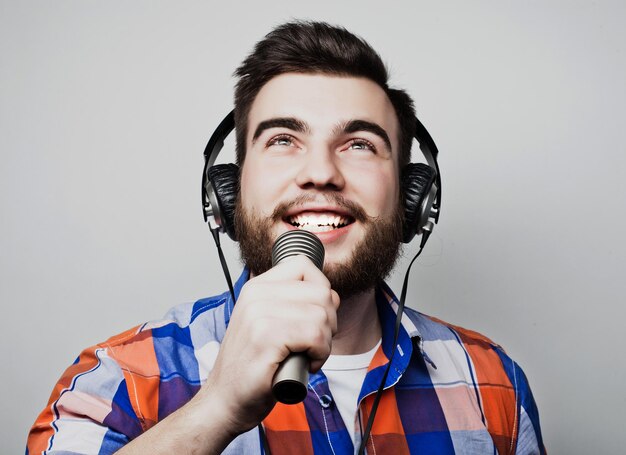 A young man with a beard wearing a shirt holding a microphone and singing, hipsterstyle.Over gray background.