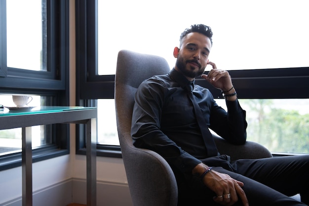 young man with a beard wearing a suit and tie sitting on a sofa looking at the camera