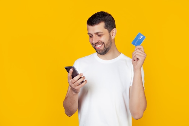 Young man with a beard in a white t-shirt holding a credit card.