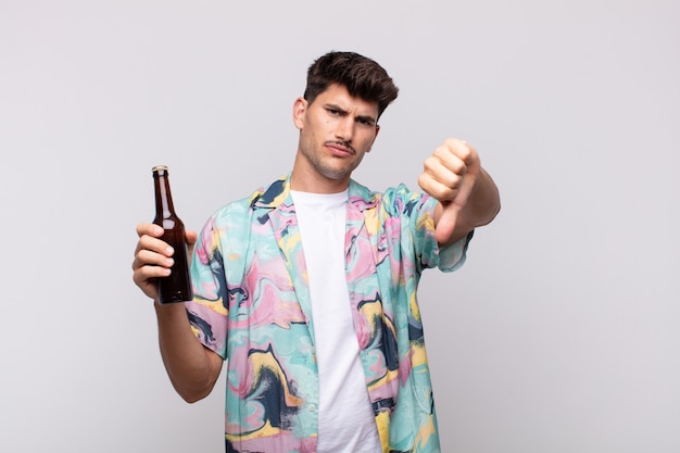 Young man with a beer feeling cross, angry, annoyed, disappointed or displeased, showing thumbs down with a serious look