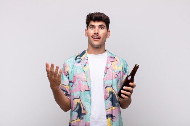 Young man with a beer feeling happy, surprised and cheerful