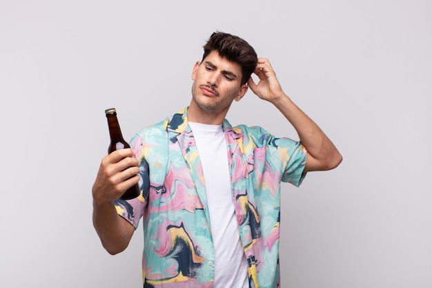 Young man with a beer feeling puzzled and confused, scratching head and looking to the side