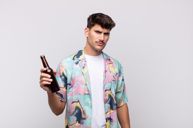 Young man with a beer feeling sad, upset or angry and looking to the side with a negative attitude, frowning in disagreement