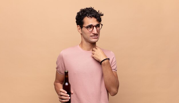 Young man with a beer feeling stressed, anxious, tired and frustrated, pulling shirt neck, looking frustrated with problem