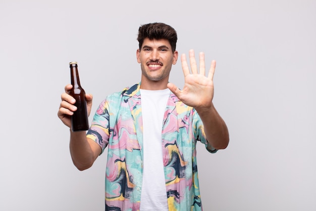 Young man with a beer smiling and looking friendly, showing number five or fifth with hand forward, counting down