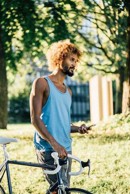 Young man with bicycle and cell phone in park