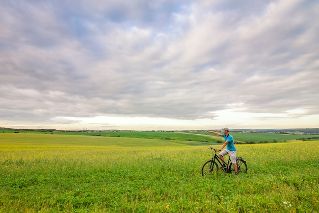 Young man with a bicycle on green field on a sunny summer day