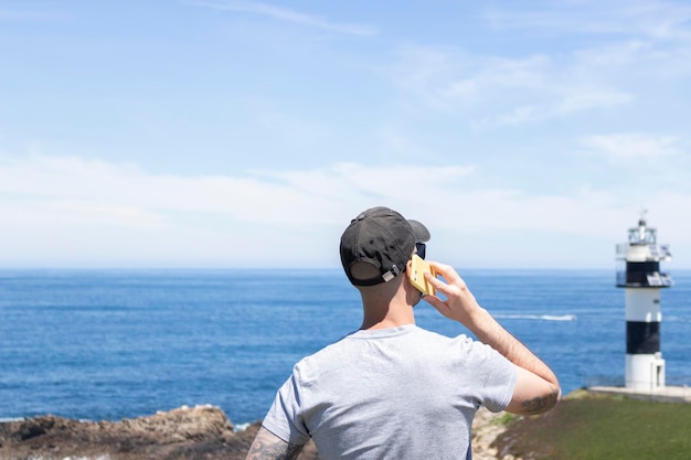 黒い帽子とサングラスをかけた若い男性が、夏休みにビーチから携帯電話で話し、コンセプト、限定フォーカス。