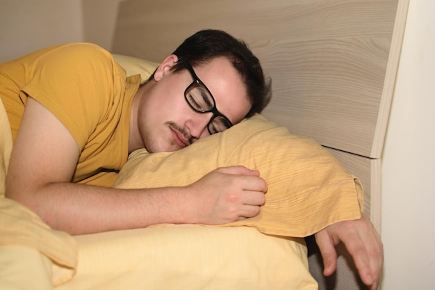 Young man with black eyeglasses sleeping turned in bed