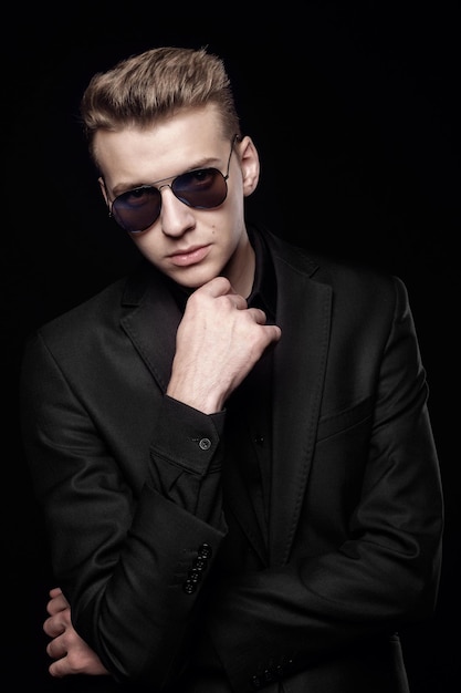 Photo young man with black glasses in black jacket on black background