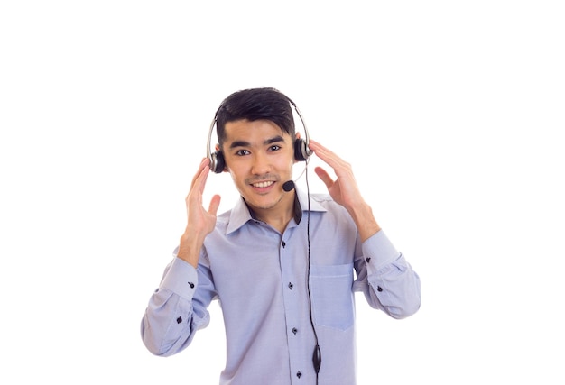 スタジオで白い背景の上の黒いヘッドフォンと青いシャツの黒い髪の若い男