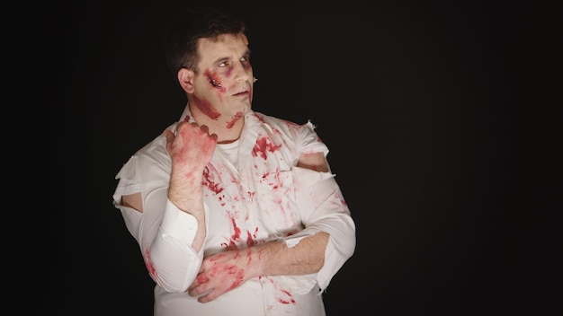 Молодой человек с кровью на лице, одетый как зомби на хэллоуин.