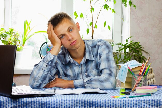 A young man with blue eyes, dressed in a plaid shirt, sits puzzled at his workplace. Education concept.