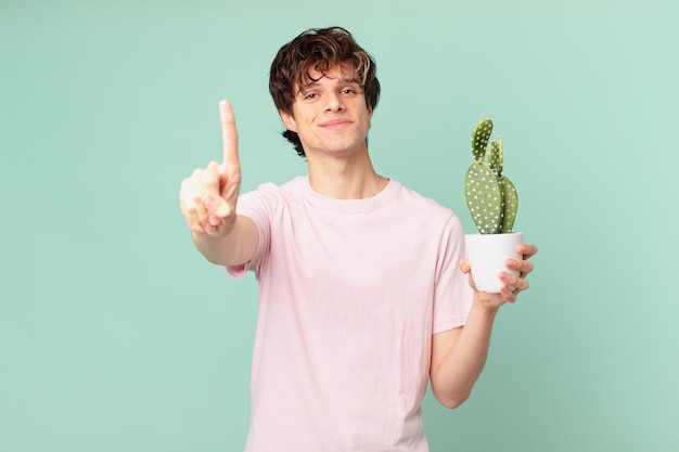 Young man with a cactus smiling and looking friendly, showing number one