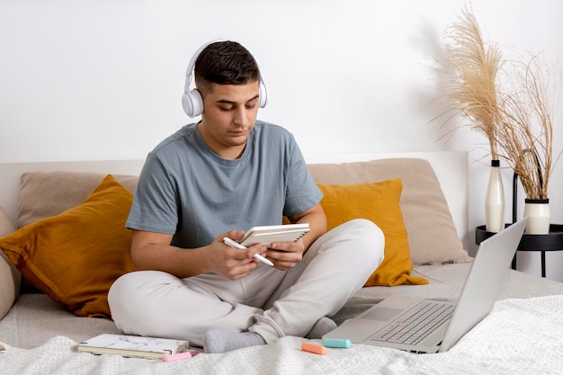 Young man with casual clothes sitting on the bed at home with laptop computer and studying Man using elearning platform to make a video call with his teacher Distance education Cosy interior