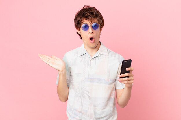 Young man with a cell phone looking surprised and shocked, with jaw dropped holding an object