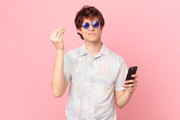 Young man with a cell phone making capice or money gesture, telling you to pay