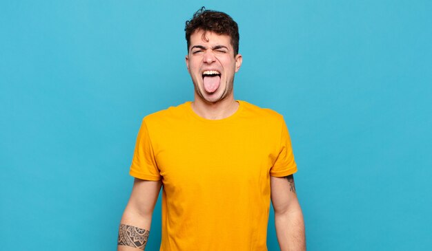 Young man with cheerful, carefree, rebellious attitude, joking and sticking tongue out, having fun