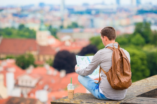 Giovane con una mappa della città e zaino. turista caucasico guardando la mappa della città europea con una splendida vista delle attrazioni.