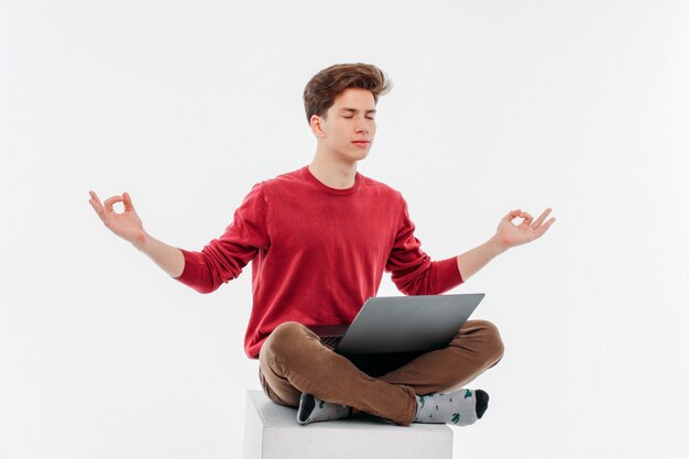 Young man with closed eyes sitting in Lotus position with laptop