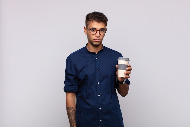 Young man with a coffee feeling sad, upset or angry and looking to the side with a negative attitude, frowning in disagreement