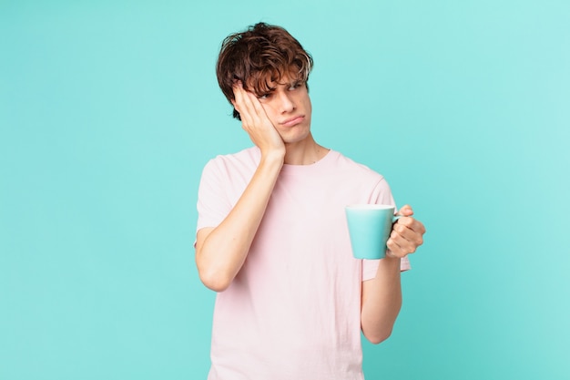 疲れた後、退屈、欲求不満、眠い感じのコーヒーマグカップを持つ若い男
