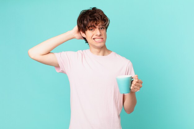 頭に手を置いて、ストレス、不安、または恐怖を感じているコーヒーマグカップを持つ若い男