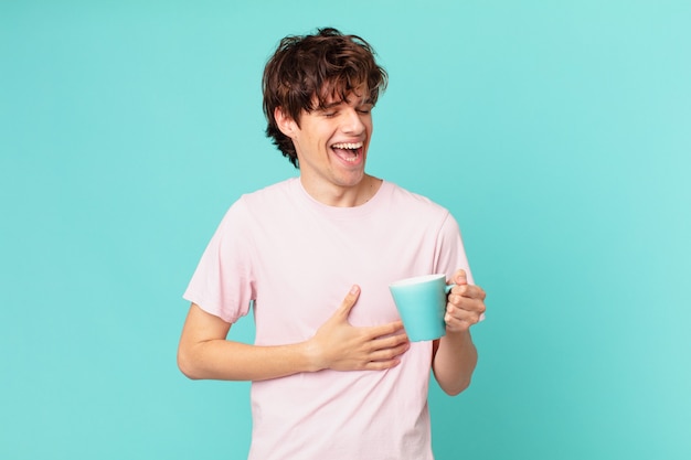 Young man with a coffee mug laughing out loud at some hilarious joke