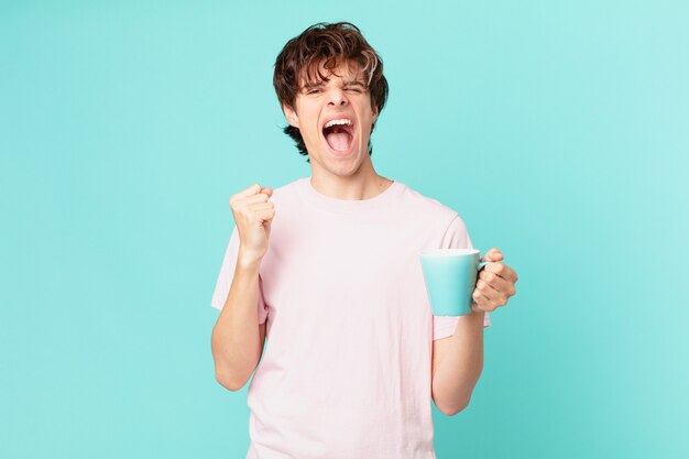 Young man with a coffee mug shouting aggressively with an angry expression