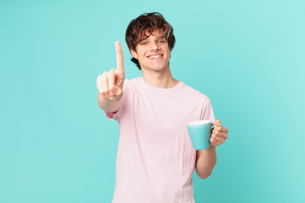 Young man with a coffee mug smiling proudly and confidently making number one