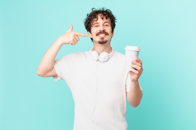 Young man with a coffee smiling confidently pointing to own broad smile