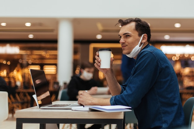 カフェのテーブルに座ってコーヒーのテイクアウトを持つ若い男。コピースペースのある写真