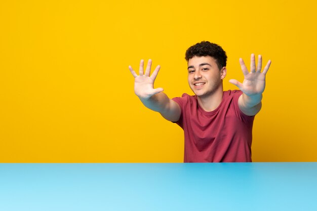 Young man with colorful wall and table counting ten with fingers