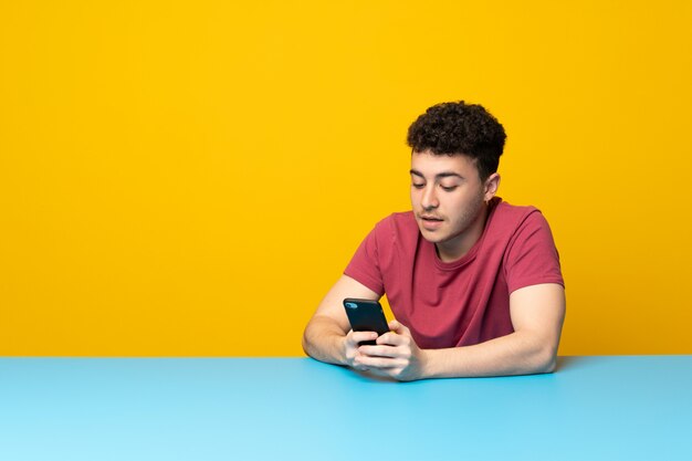 Young man with colorful wall and table sending a message with the mobile