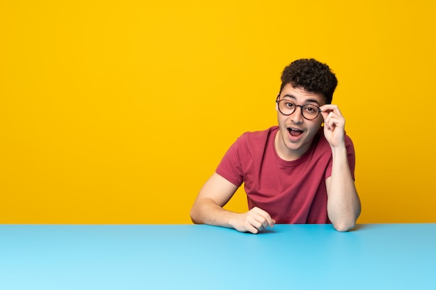 Young man with colorful wall and table with glasses and surprised