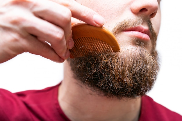 Young man with comb brushing his beard and moustache on white