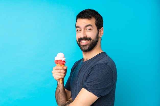 Young man with a cornet ice cream over blue with arms crossed and looking forward