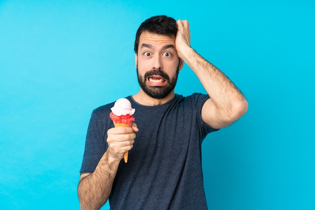 Young man with a cornet ice cream over isolated blue wall frustrated and takes hands on head