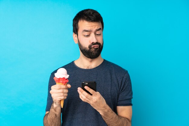 Young man with a cornet ice cream over isolated blue wall thinking and sending a message