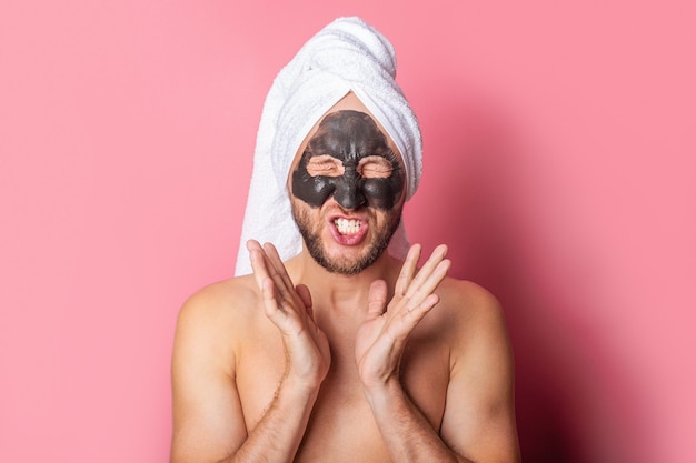 Young man with cosmetic mask with closed eyes on a pink background
