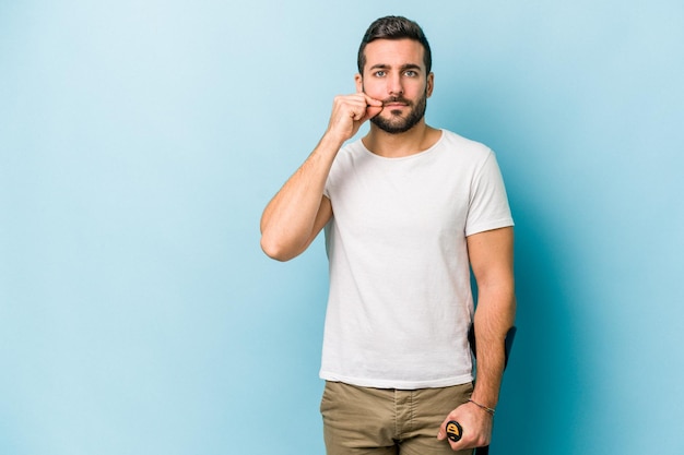 Young man with crutches isolated on blue background with fingers on lips keeping a secret