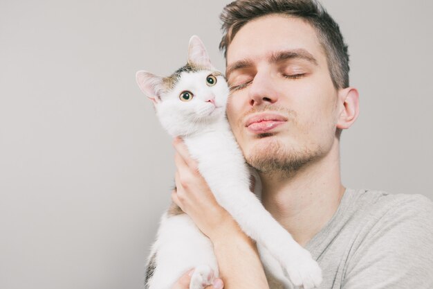 Young man with cute funny cat on light background