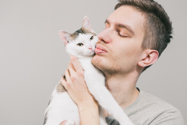 Young man with cute funny cat on light background