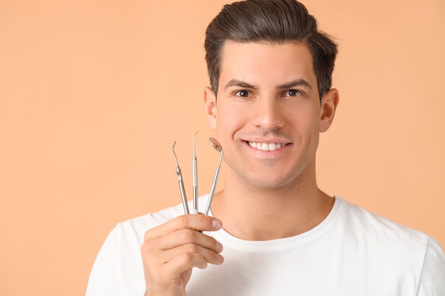 Young man with dental tools on color